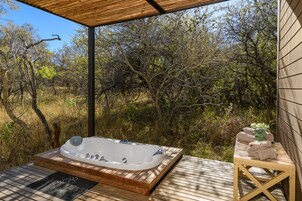 Una terraza de madera con un jacuzzi, una mesa de madera con toallas y vistas a un paisaje natural.