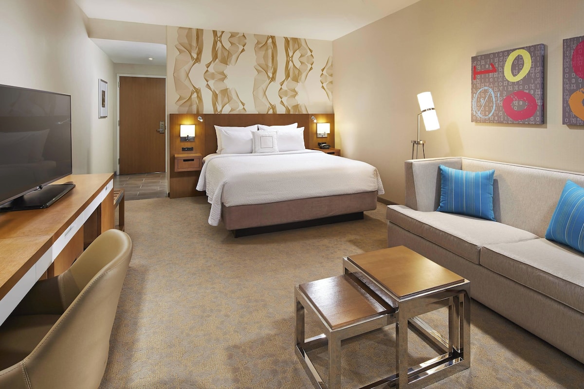 Quarto de hotel com cama, televisão, sofá, mesa de centro e escrivaninha.