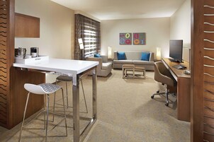 Una habitación de hotel moderna con kitchenette, zona de comedor, sofá y televisión.