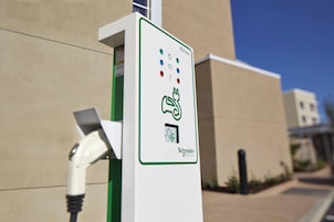 Uma estação de carregamento EVLink com interface verde, um plugue e o logotipo da Schneider Electric.