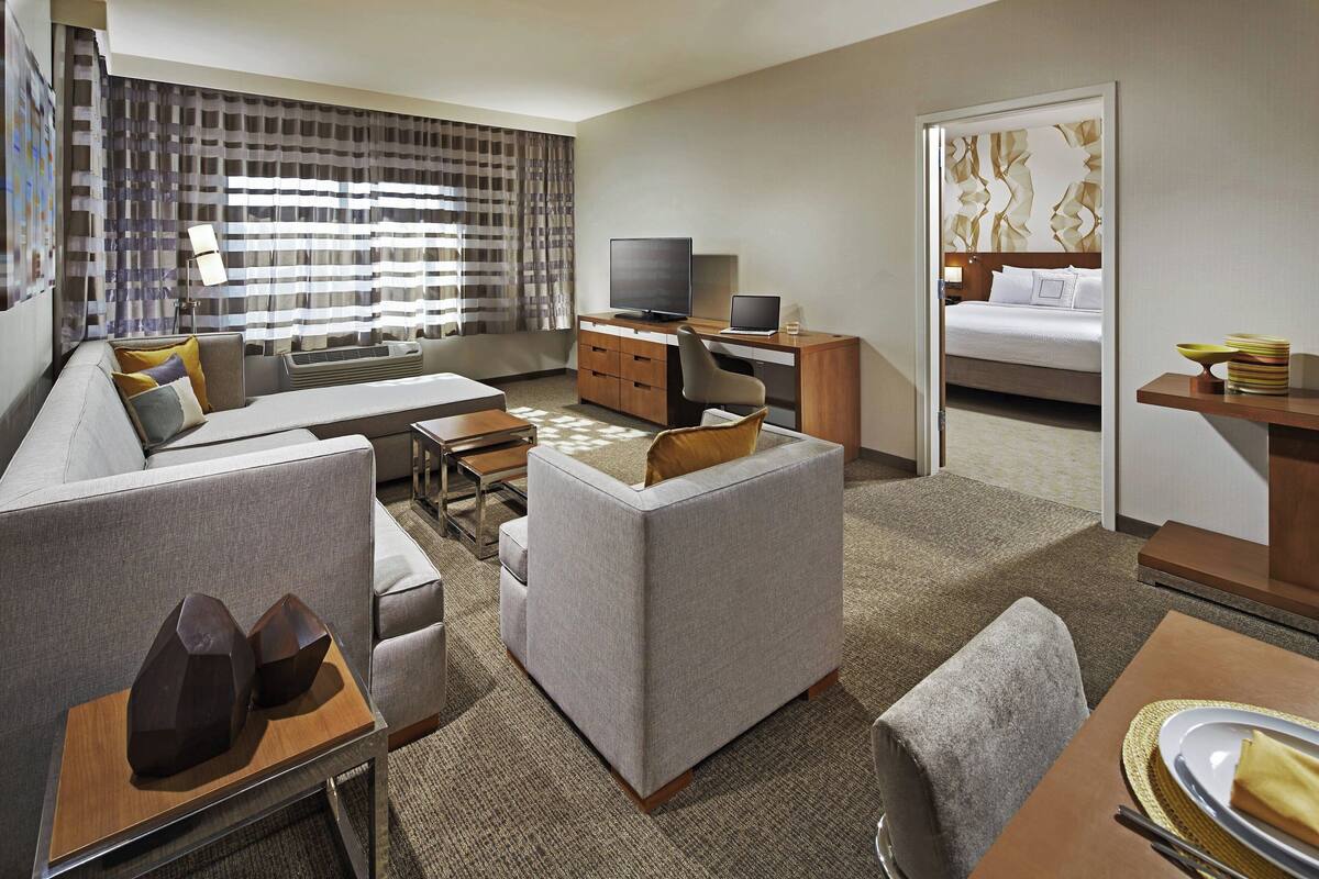 Quarto de hotel moderno com sofá, mesa de jantar, televisão, laptop e cama.