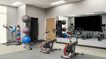 Een fitnessruimte met hometrainers, fitnessballen en een loopband.