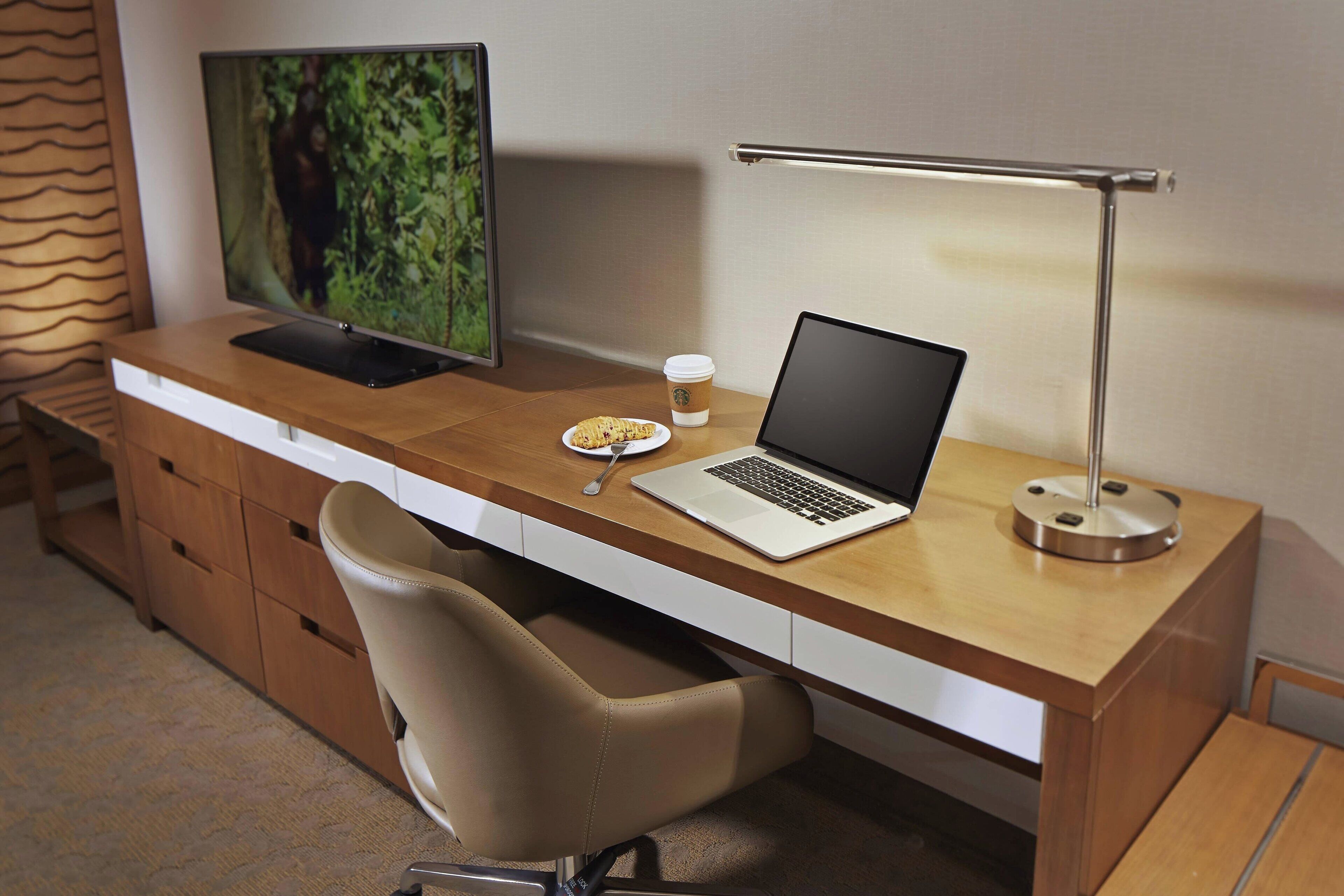 A modern workspace with a wooden desk, a laptop, a monitor, a coffee cup, and a chair.