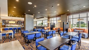 A modern restaurant with blue and orange seating, a bar area, and large windows offering a view of the outdoors. - Courtyard St. Petersburg Clearwater/Madeira Beach (Madeira Beach)