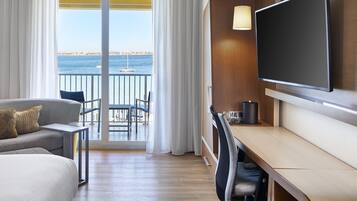 A hotel room with a balcony, a bed, a desk, a chair, and a TV.