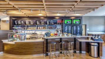 A modern bar area with a wooden counter, stools, and a menu board.