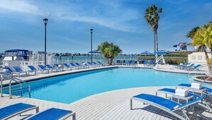 A pool area with blue lounge chairs, a wooden deck, and palm trees. - Courtyard St. Petersburg Clearwater/Madeira Beach (Madeira Beach)