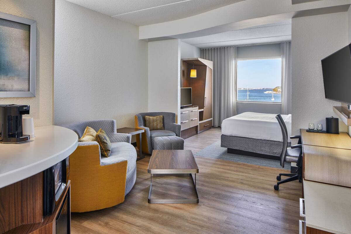A modern hotel room with a sofa, a desk, a bed, and a view of the sea.