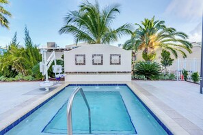 A swimming pool with a metal ladder, surrounded by palm trees and a white wall with three framed pictures. - Courtyard St. Petersburg Clearwater/Madeira Beach (Madeira Beach)
