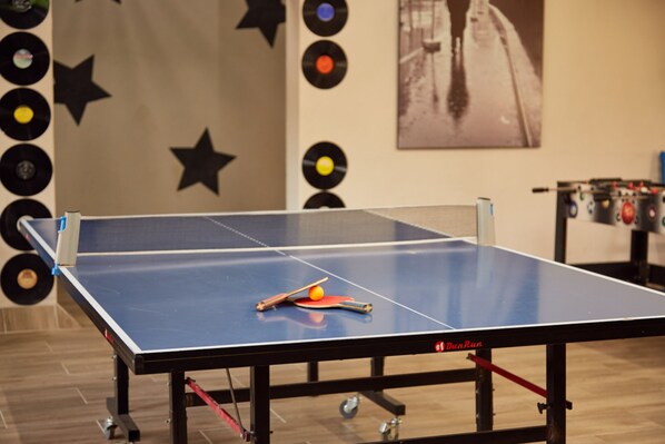 A ping pong table with a ball and paddle in the center, surrounded by a wall decorated with vinyl records and stars. - First Group Magalies Park (Hartbeespoort)