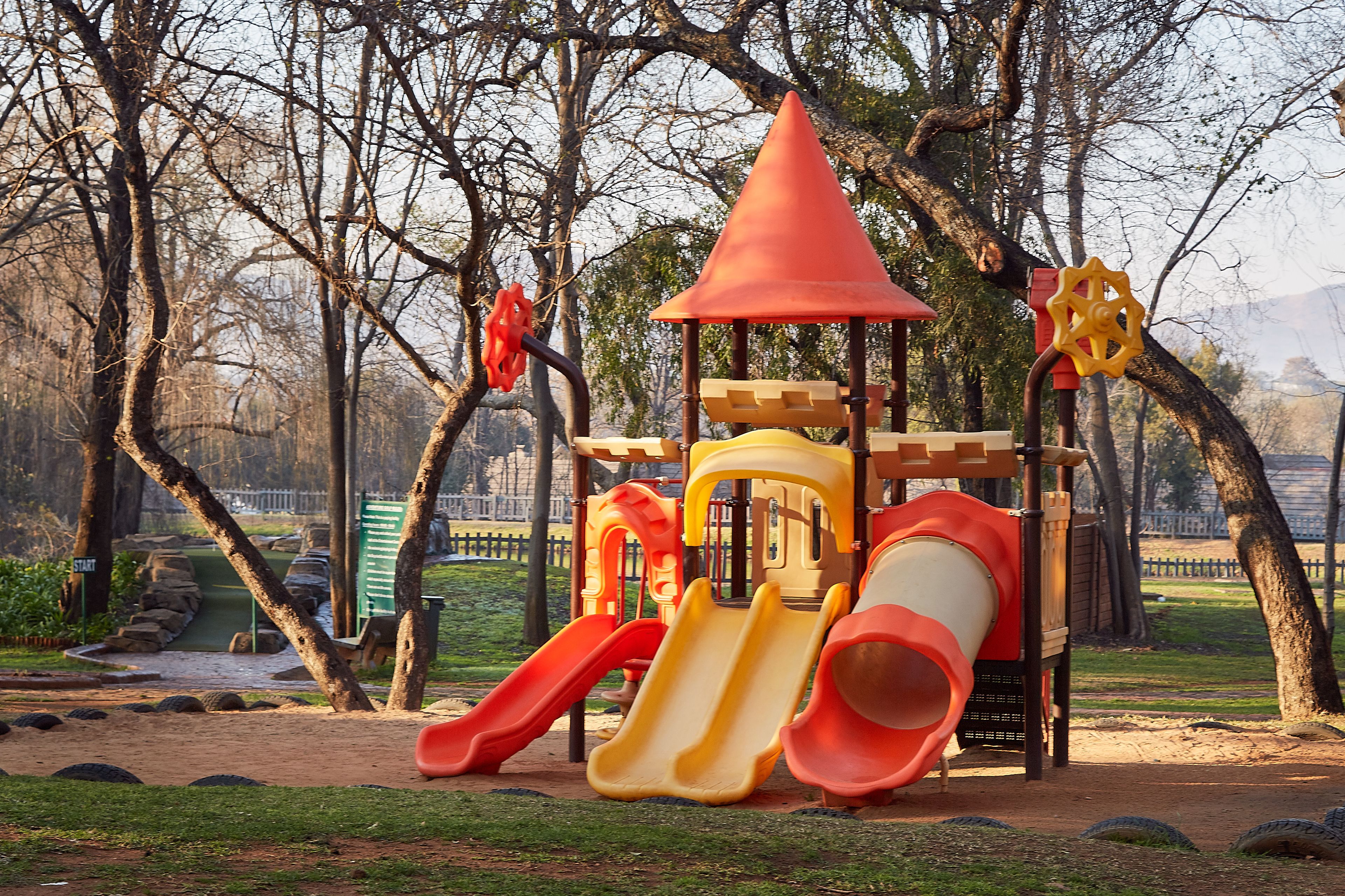 Un parque infantil con toboganes y estructuras para escalar, rodeado de árboles.