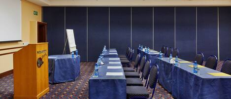A conference room with a long table, chairs, a podium, and a projector screen.