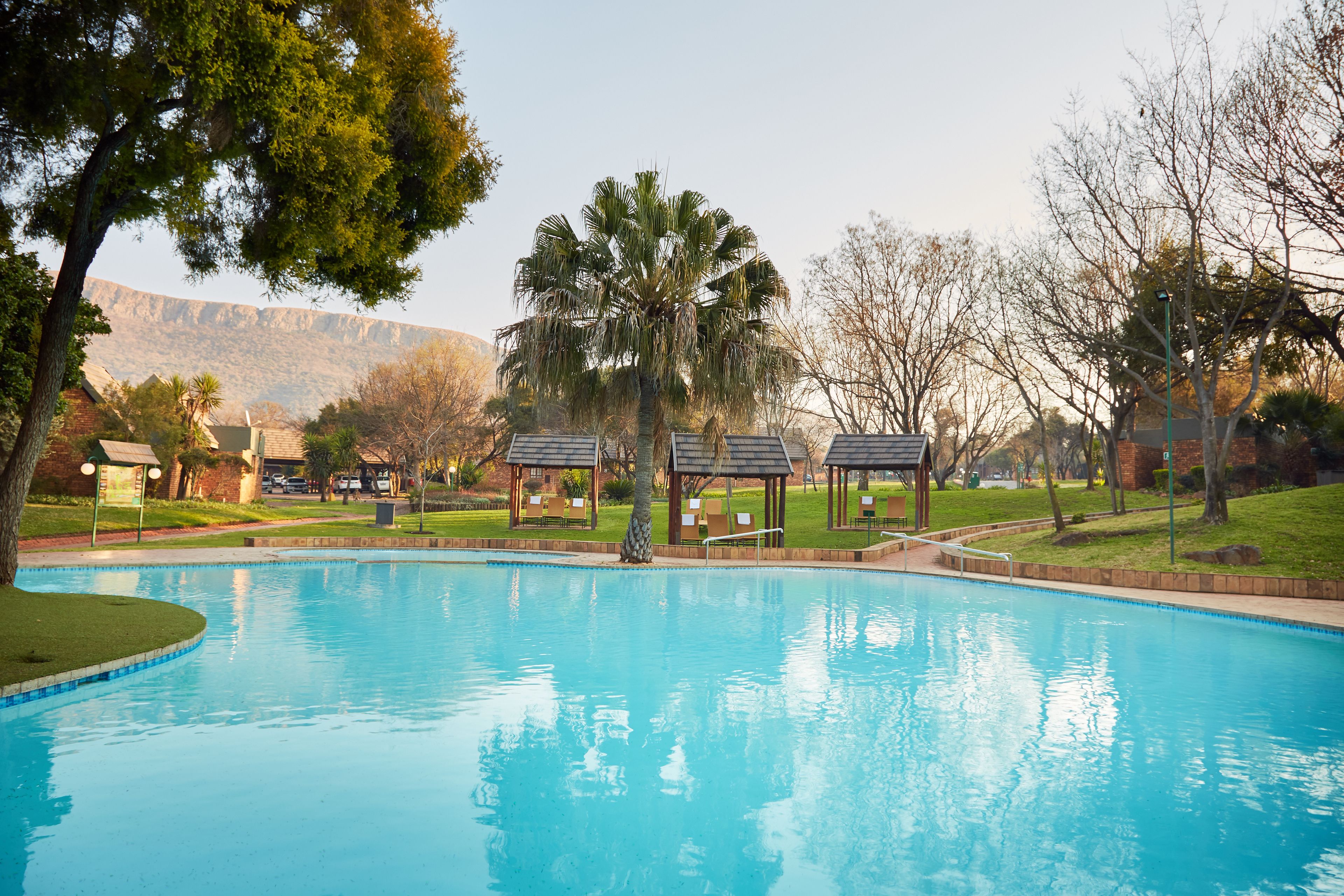 A swimming pool with lounge chairs and gazebos, surrounded by trees and a view of mountains.