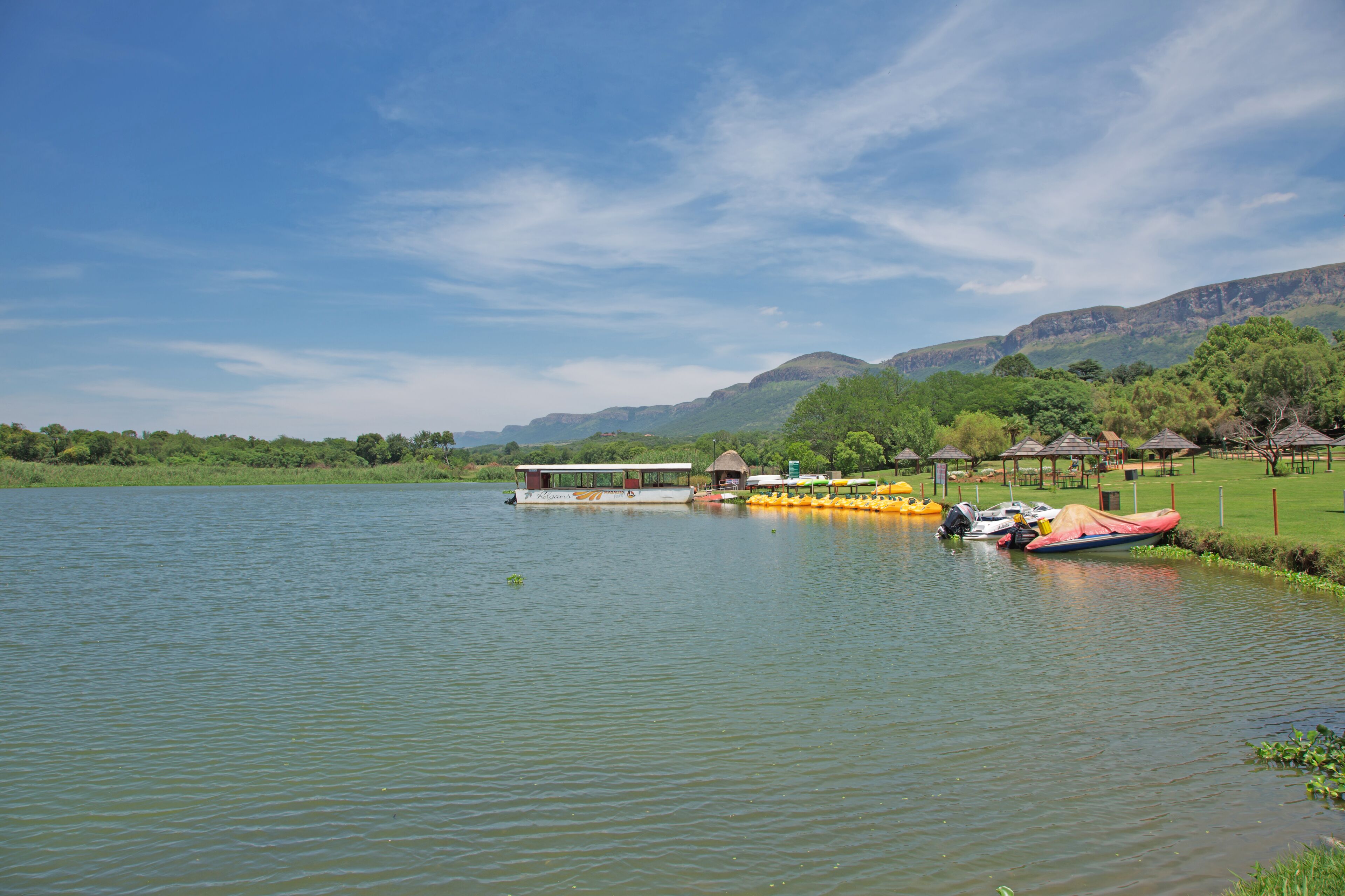 A lakeside view with a boat docked near a grassy area and a small pavilion.