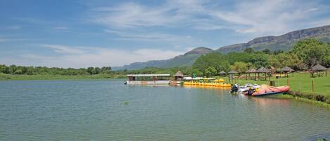 A lakeside view with a boat docked near a grassy area and a small pavilion.