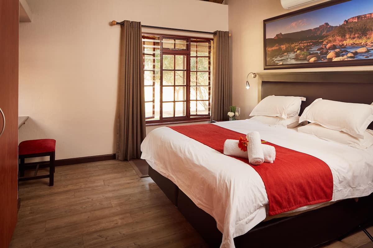 Une chambre d’hôtel avec un grand lit, une fenêtre avec des rideaux, un tableau au mur et un plancher en bois.