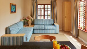 Una habitación con sofá modular, una mesa de comedor con sillas, un aparador de madera y una ventana con cortinas.