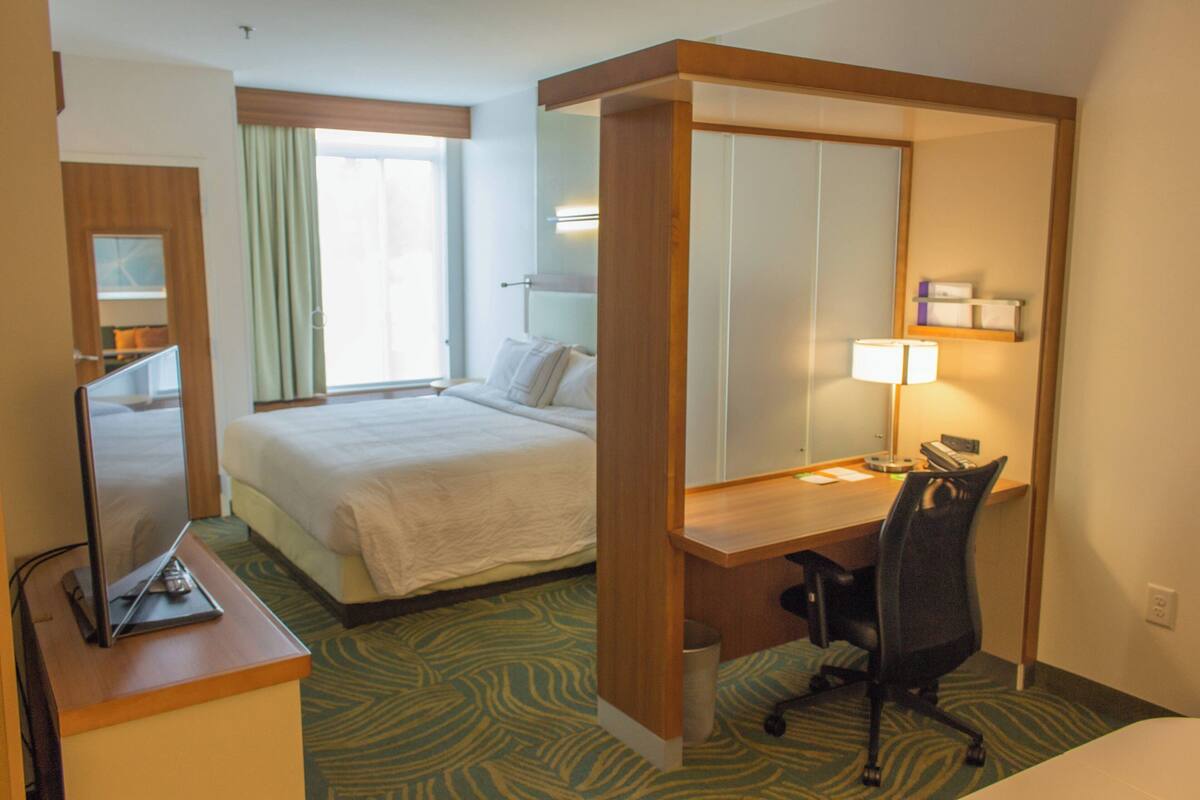 A hotel room with a bed, desk, chair, and a television on a stand.