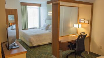 Una habitación de hotel con cama, escritorio, silla y televisor sobre un soporte.