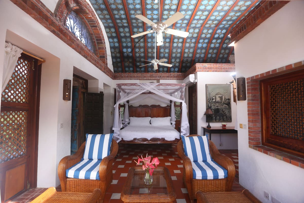 A room with a bed, two striped sofas, a ceiling fan, and a decorative ceiling.