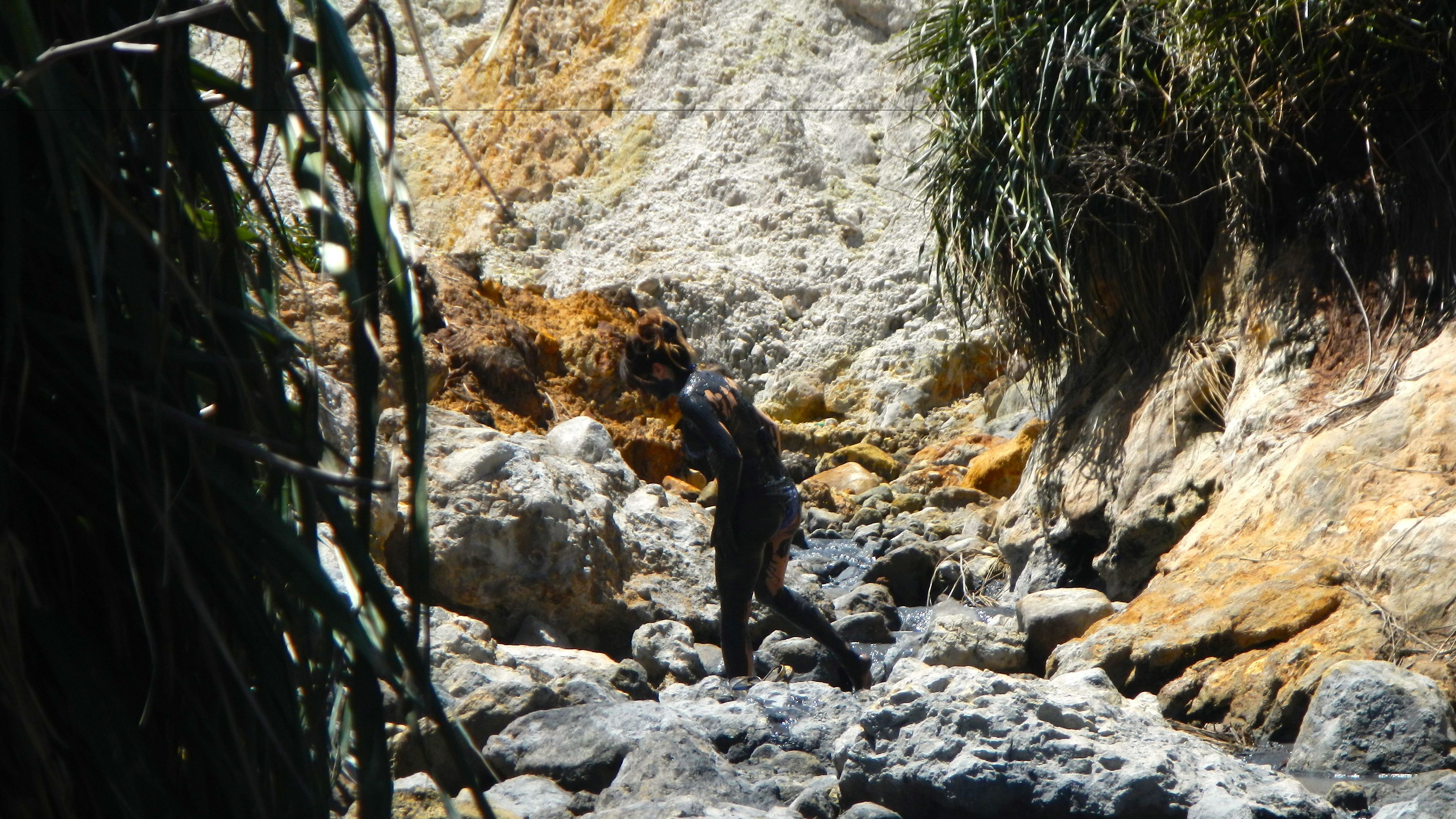 Terreno rocoso con una persona de pie entre grandes rocas y vegetación escasa.
