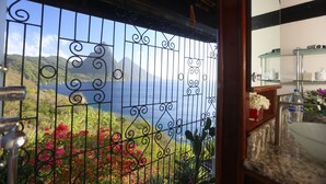 Un balcon doté d’une grille en fer forgé, une vue sur la mer et une étagère sur laquelle sont disposés divers objets.