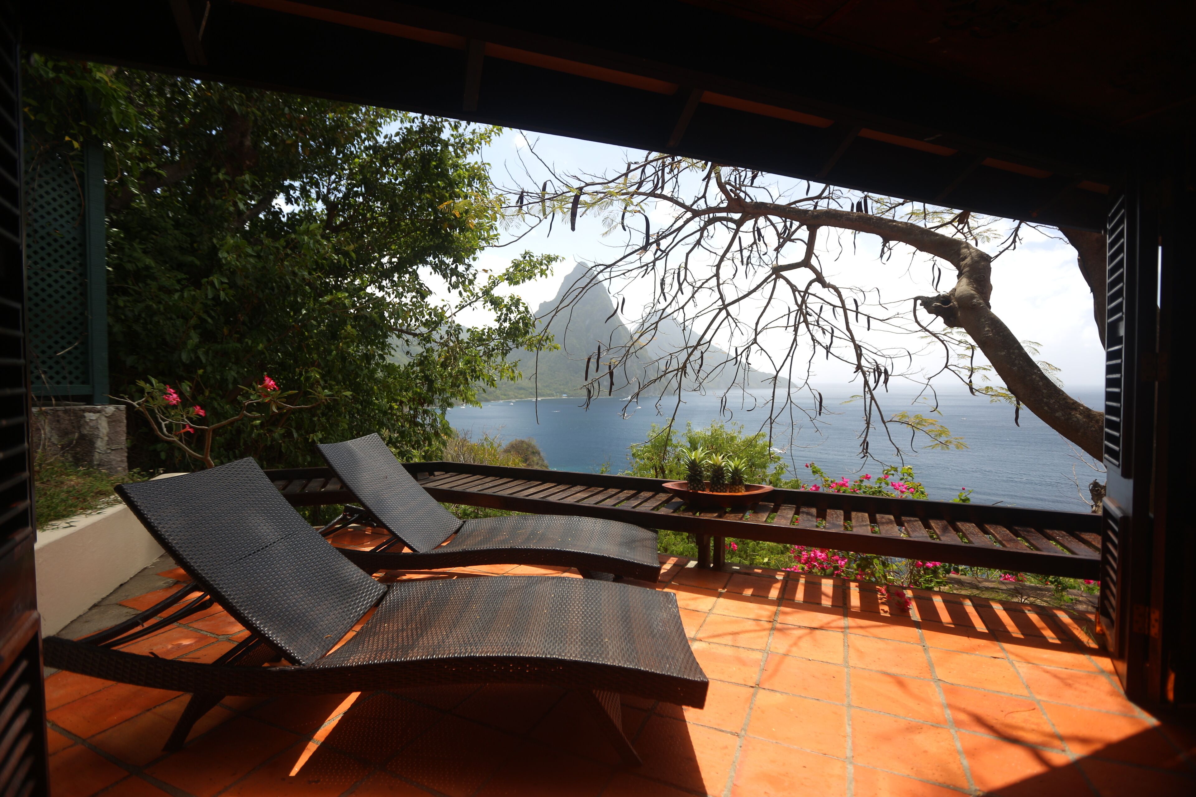 A terrace with two lounge chairs and a table, overlooking a scenic view of a mountain and a body of water.