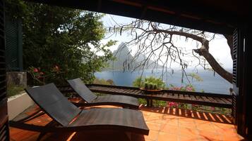 A terrace with two lounge chairs and a table, overlooking a scenic view of a mountain and a body of water.