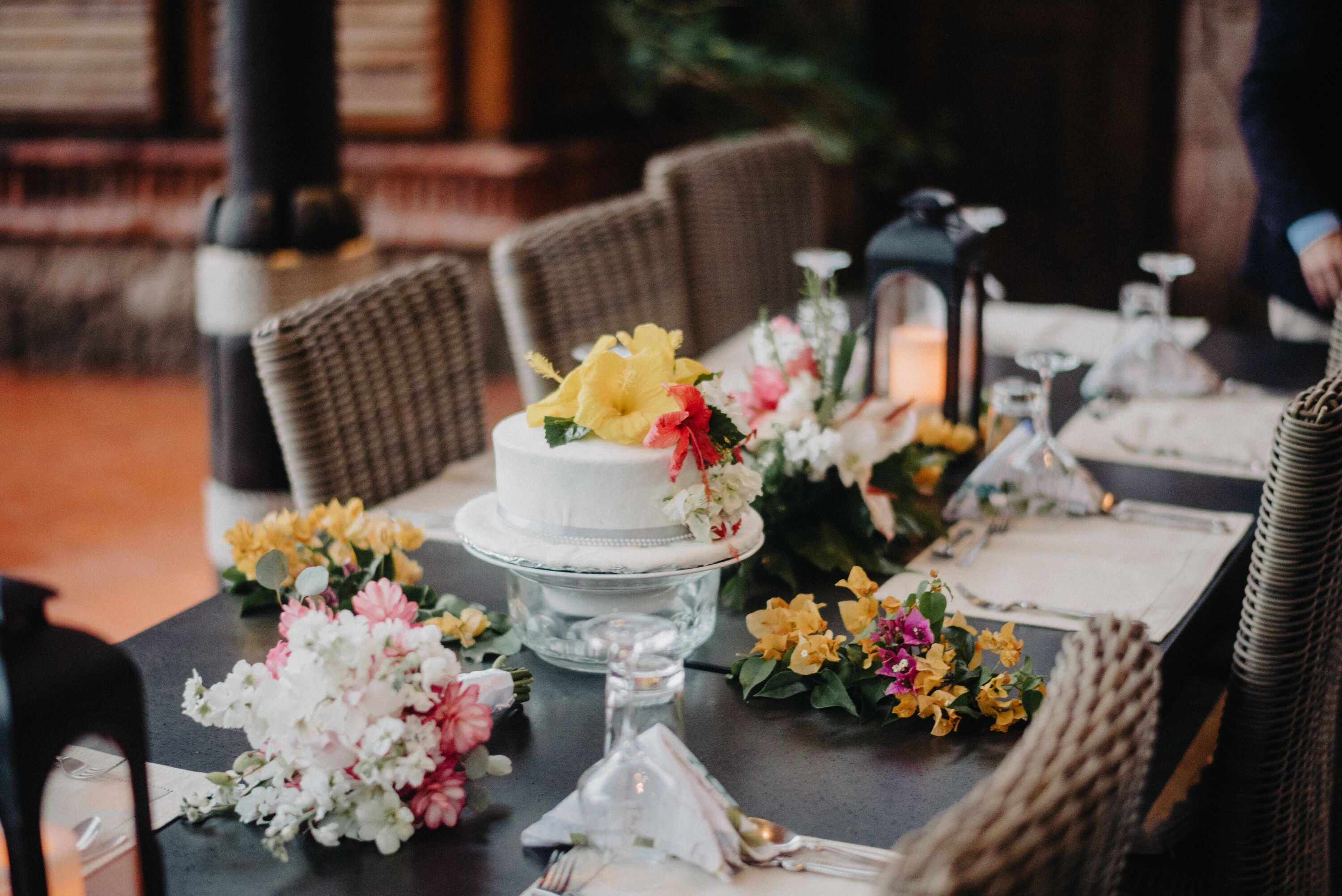 Een eettafel gedekt met een witte taart, bloemstukken en netjes gerangschikt servies.