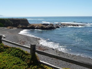 A coastal landscape with a rocky shoreline, waves crashing onto the beach, and a wooden fence in the foreground.