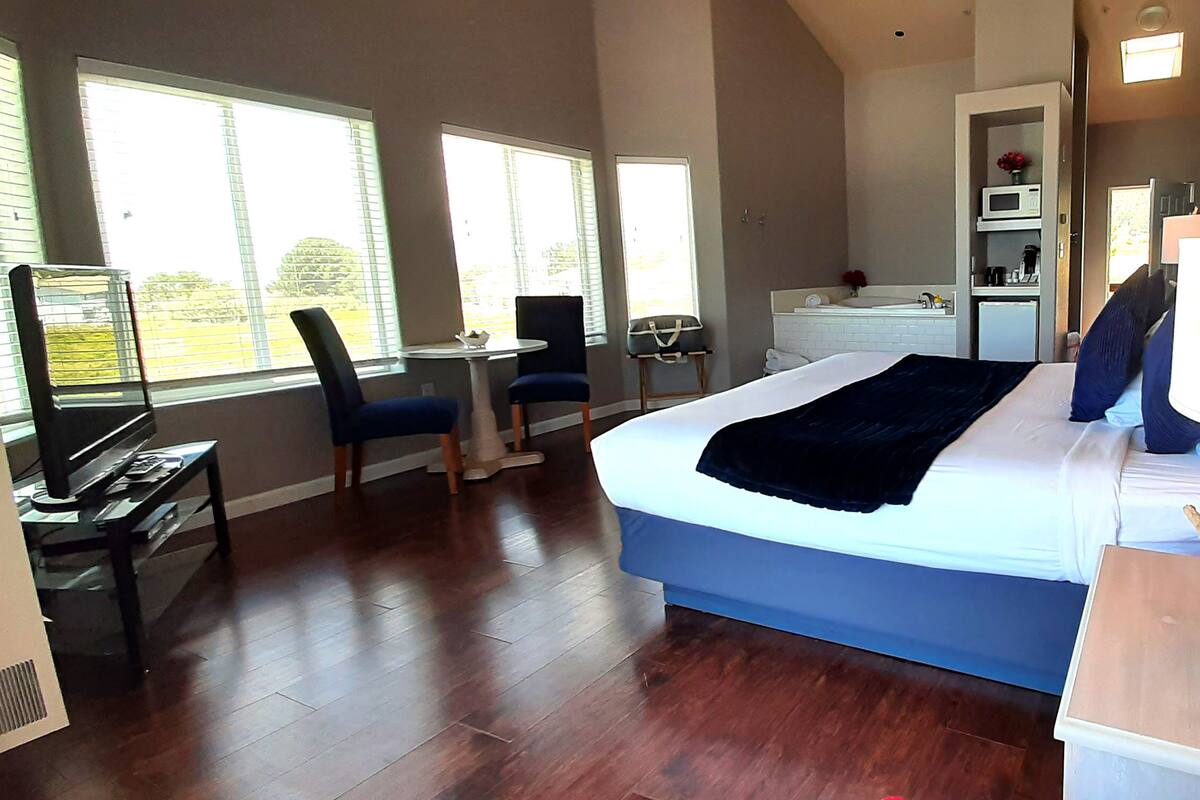 A bedroom with a bed, a desk, a chair, a lamp, and a view of the outdoors.
