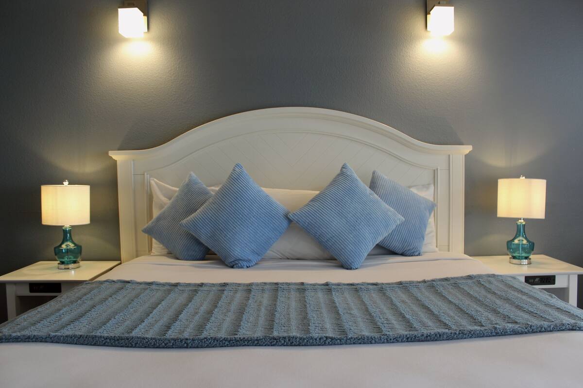 A neatly made bed with a blue knitted throw, two matching pillows, and two bedside lamps on white nightstands.