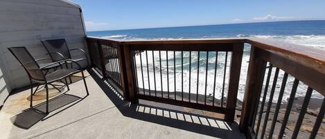 A balcony with metal chairs and a wooden railing overlooking the ocean.