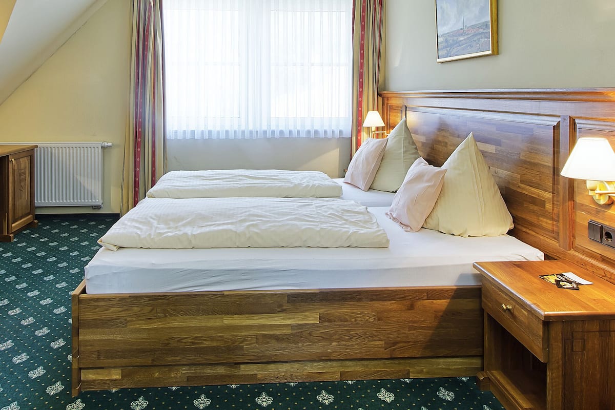 A hotel room with a wooden bed, two bedside tables, a desk with a chair, a television, and a window with curtains.
