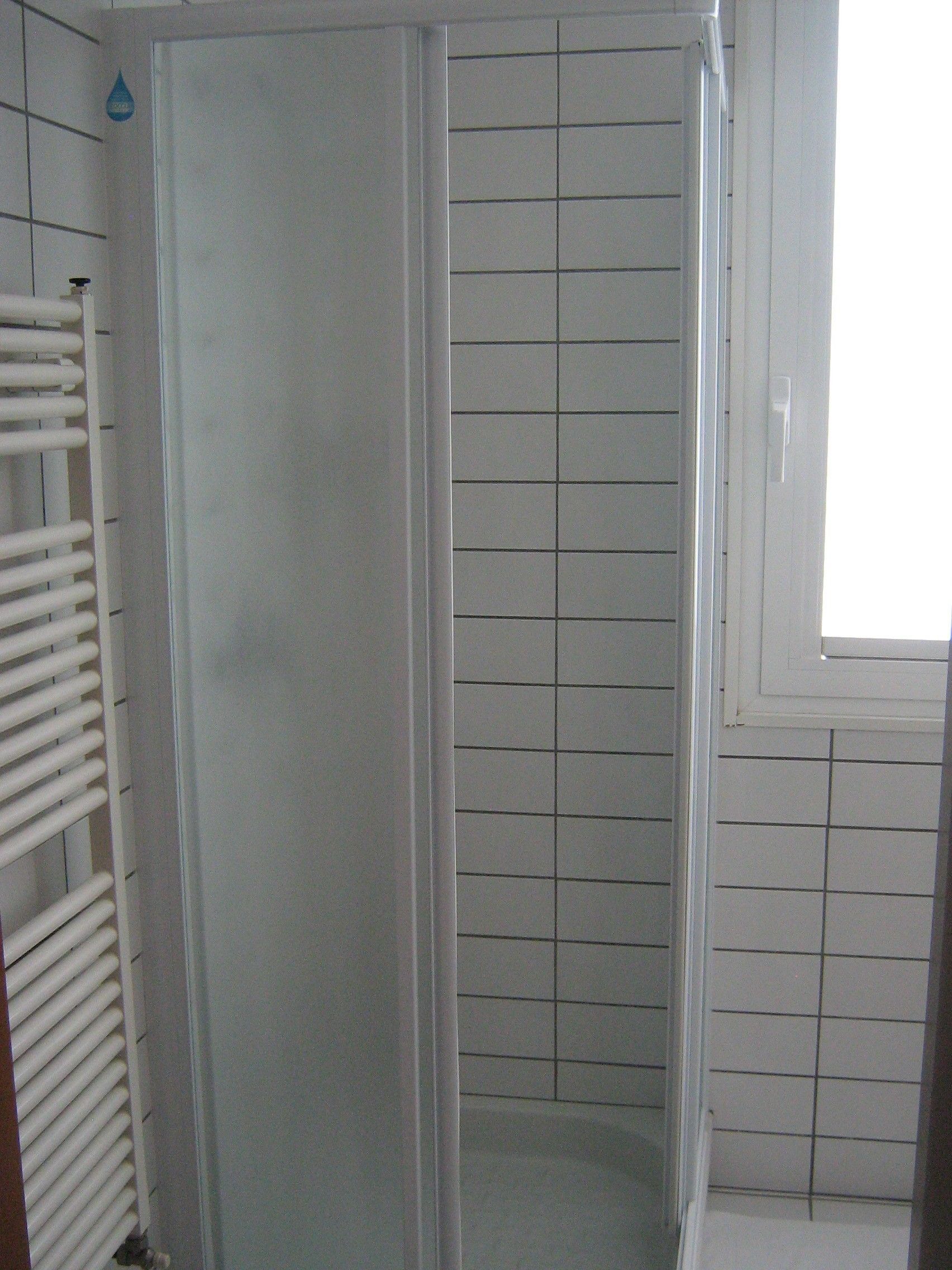 A bathroom with a shower enclosure, a white tiled wall, and a window.