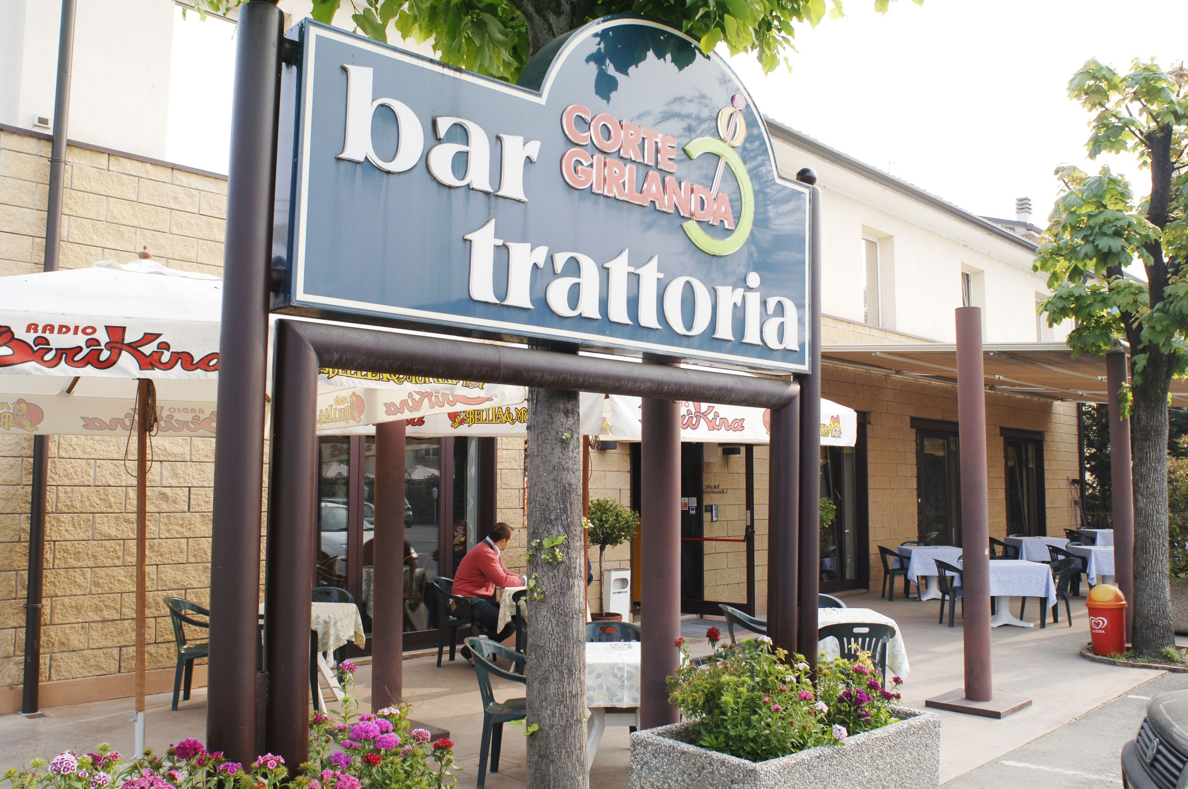 Un bar llamado "bar trattoria" con mesas al aire libre y un letrero arriba.