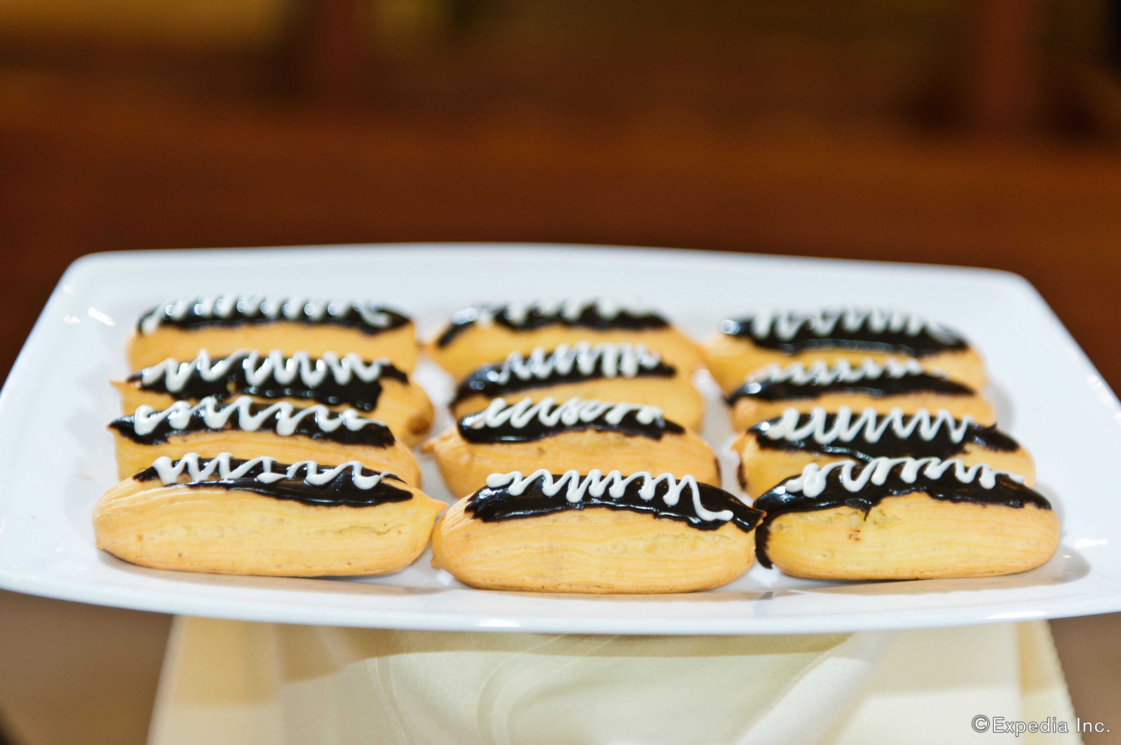 A white plate with six cream puffs topped with chocolate and white icing.