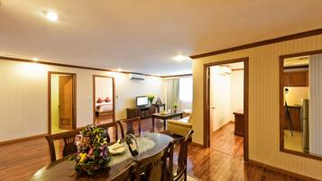 Quarto de hotel com área de refeições, televisão, pequena cozinha e banheiro visível por uma porta aberta.