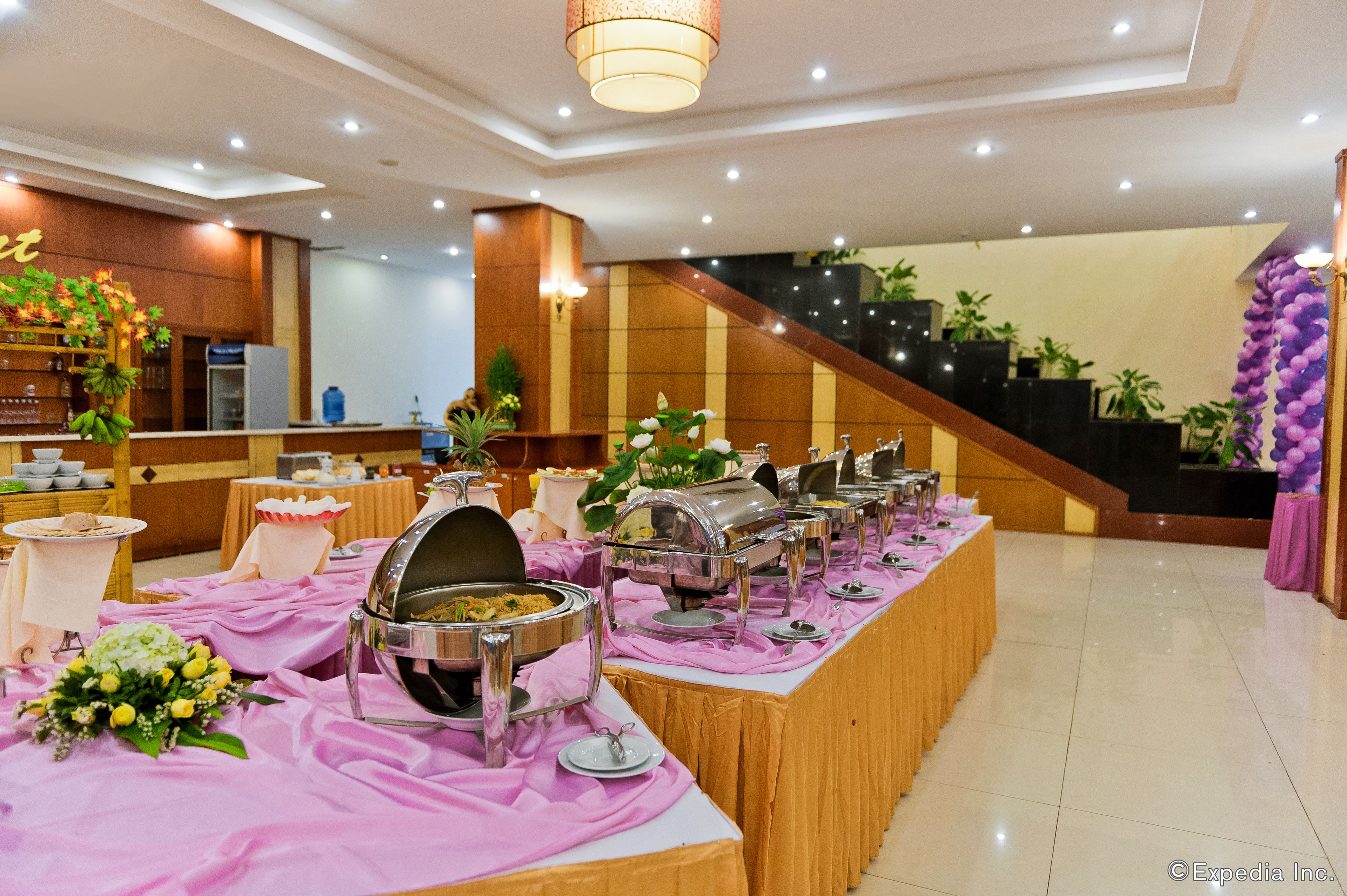 Un buffet avec plusieurs points de service, un espace d’accueil doté d’un comptoir et de plantes, et un escalier menant à un niveau supérieur.