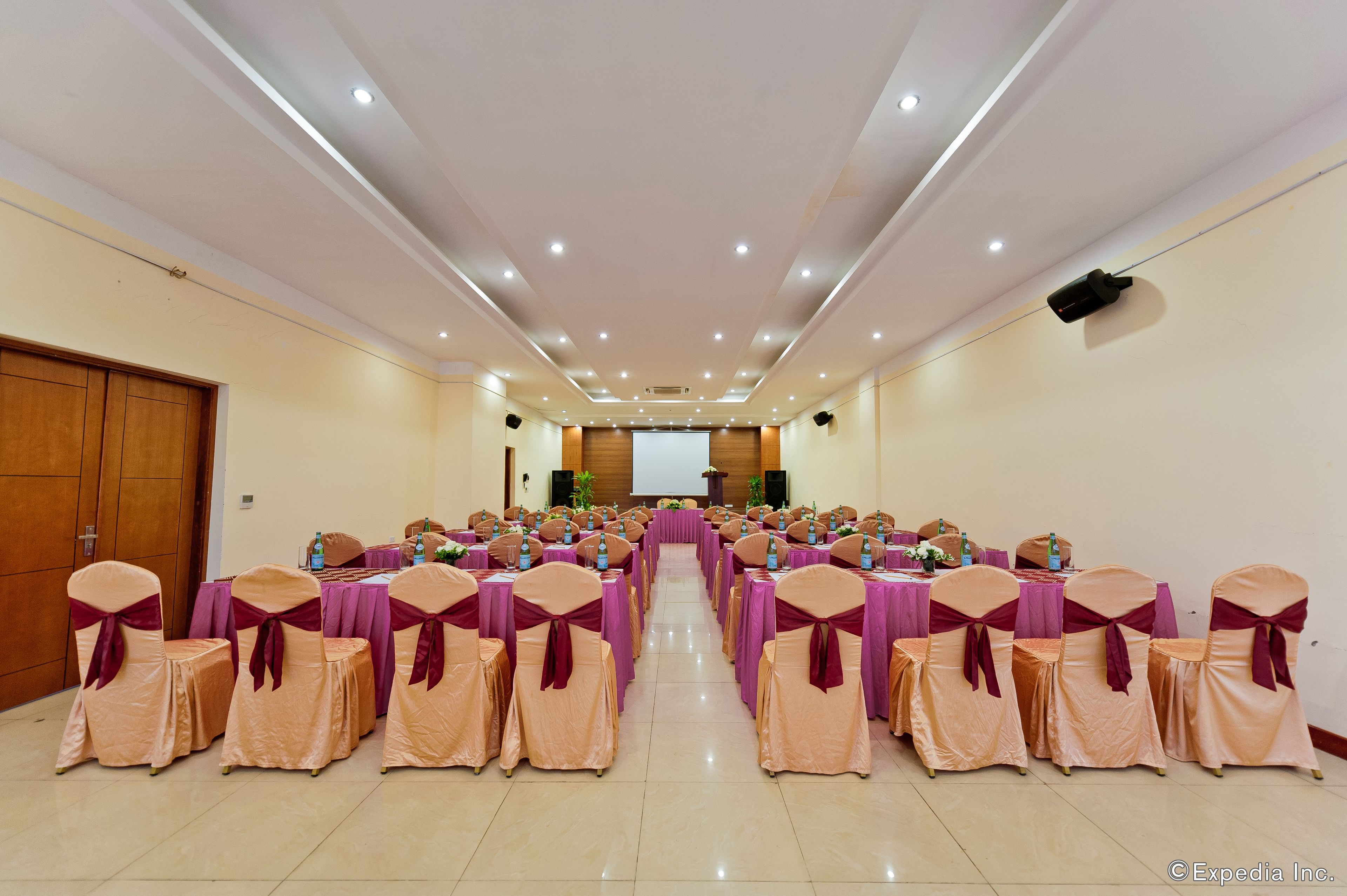 A conference room with rows of tables and chairs, equipped with microphones and projectors, suggesting a formal meeting or event setup.