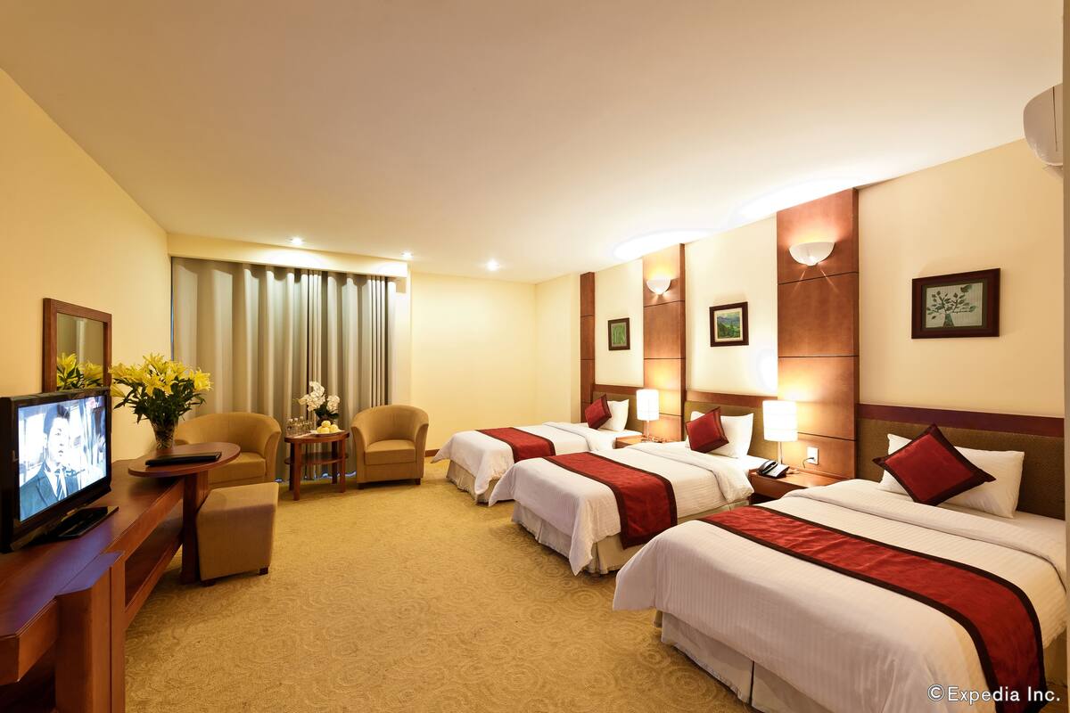 A hotel room with two beds, a TV, a sofa, and a desk with a lamp.
