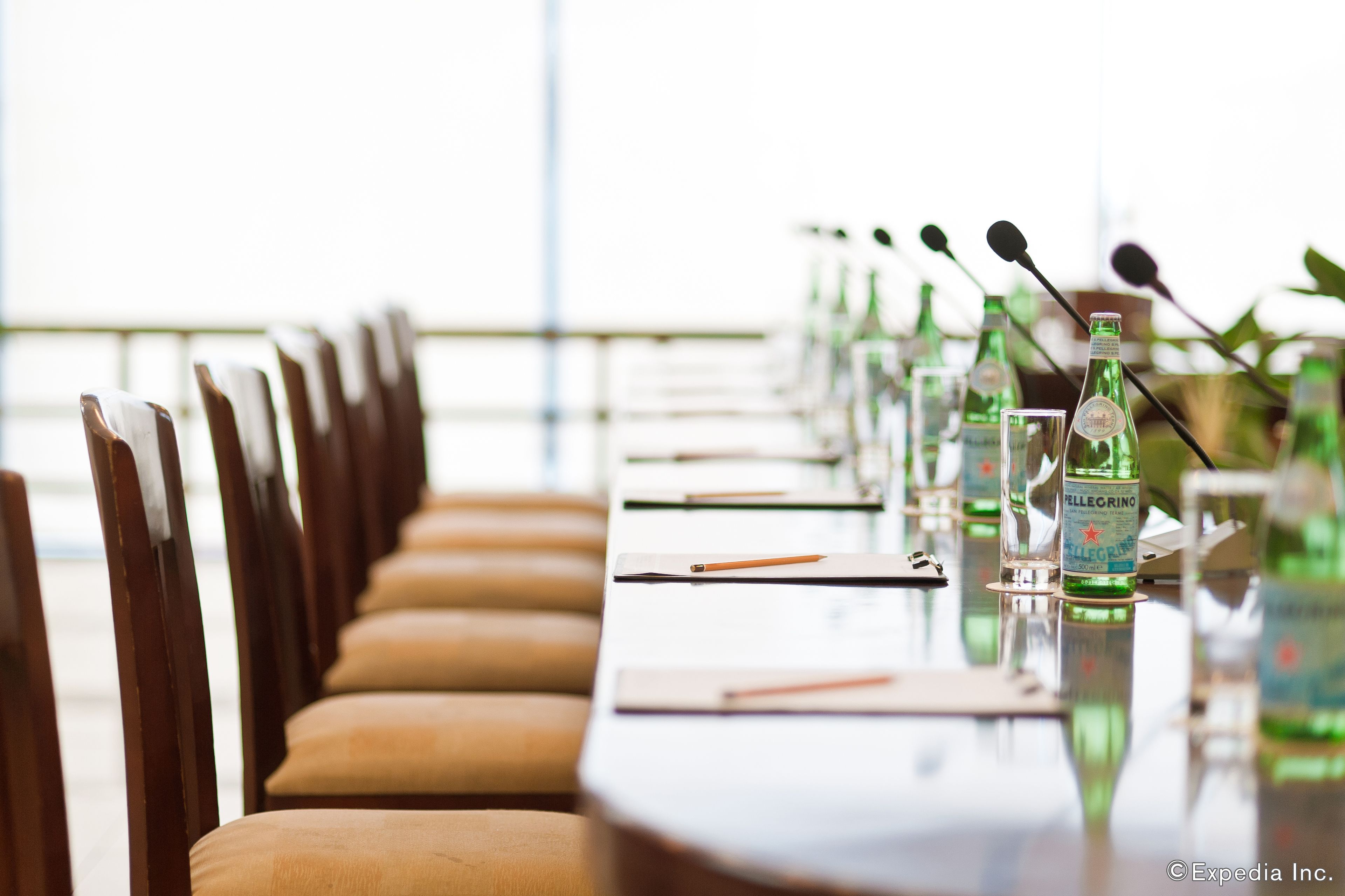 Un salón de conferencias con una larga mesa, sillas, micrófonos y botellas de agua Pellegrino.