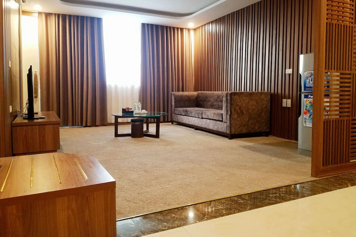 A modern living room with a glass coffee table, a sofa, a wooden desk, and a refrigerator.