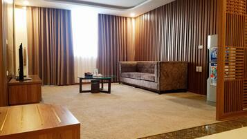 A modern living room with a glass coffee table, a sofa, a wooden desk, and a refrigerator.
