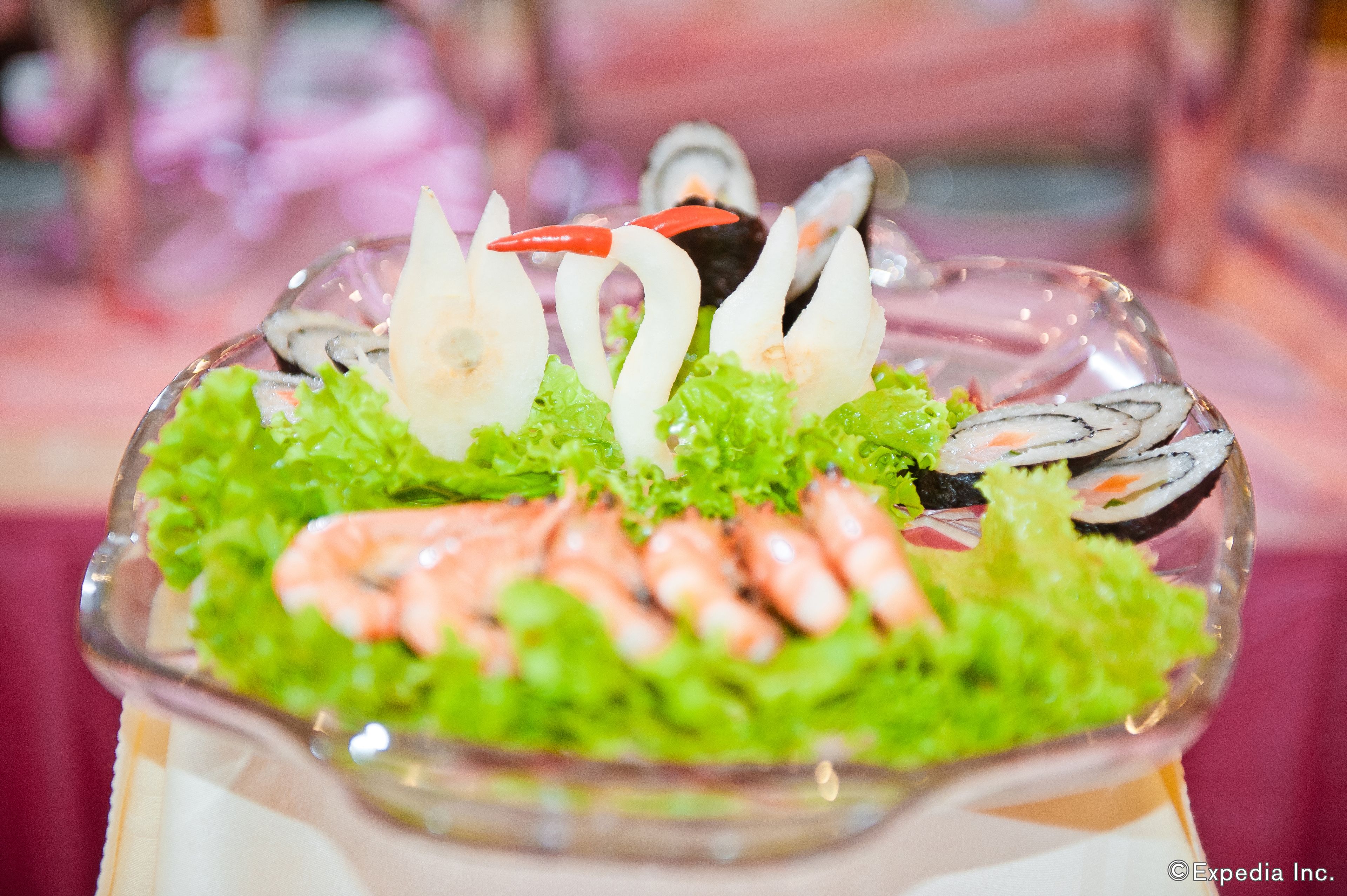 A glass bowl containing sushi, shrimp, and lettuce.