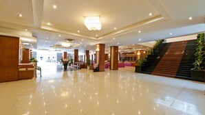 A spacious lobby with a polished floor, a reception desk, and a staircase leading to a restaurant area. - Muong Thanh Dien Chau Hotel (Dien Chau)