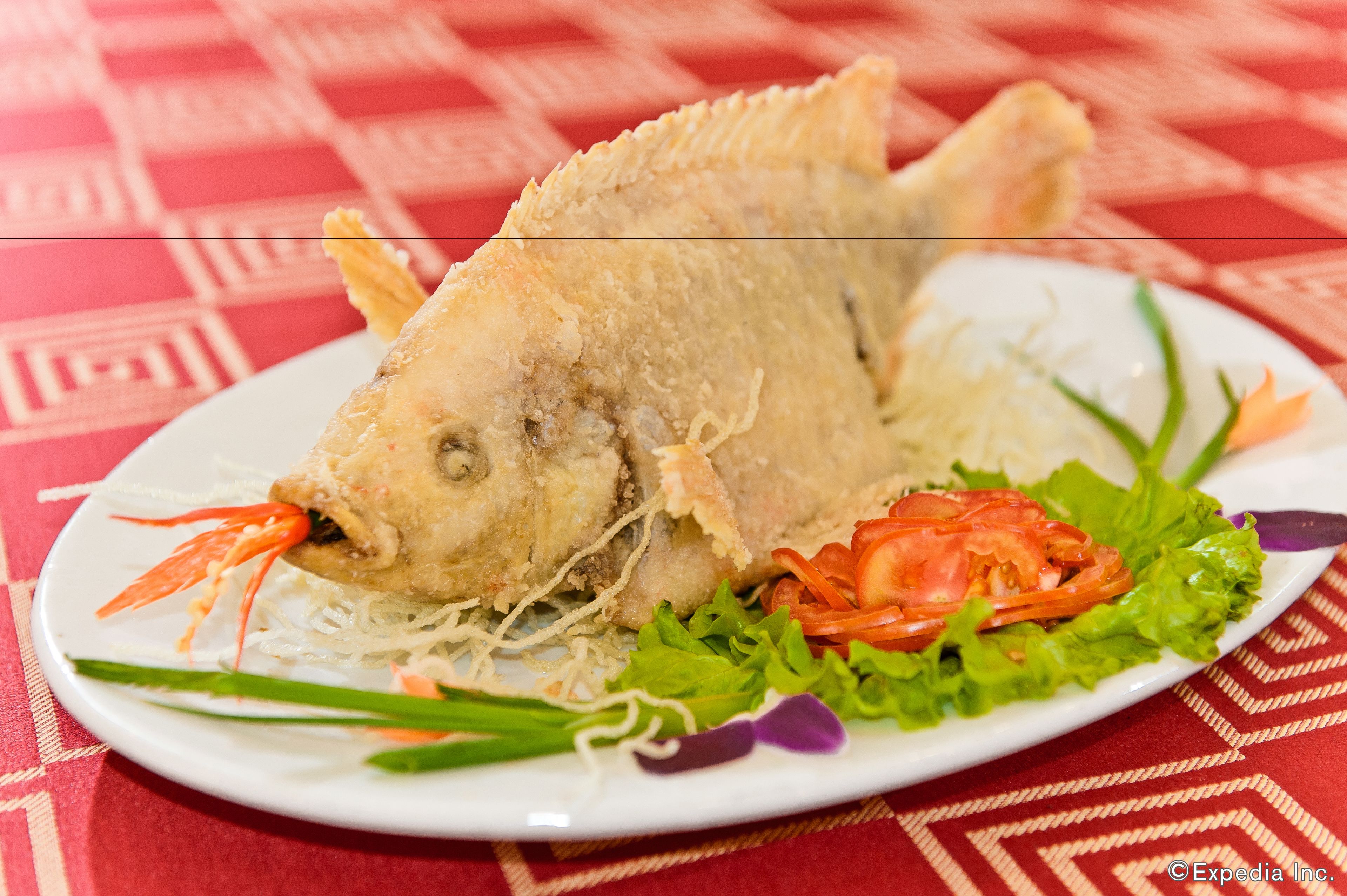 Un plato con pescado frito, lechuga y rodajas de tomate.