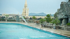 A swimming pool with a water fountain, outdoor seating, and a view of a historic building in the background. - Muong Thanh Dien Chau Hotel (Dien Chau)