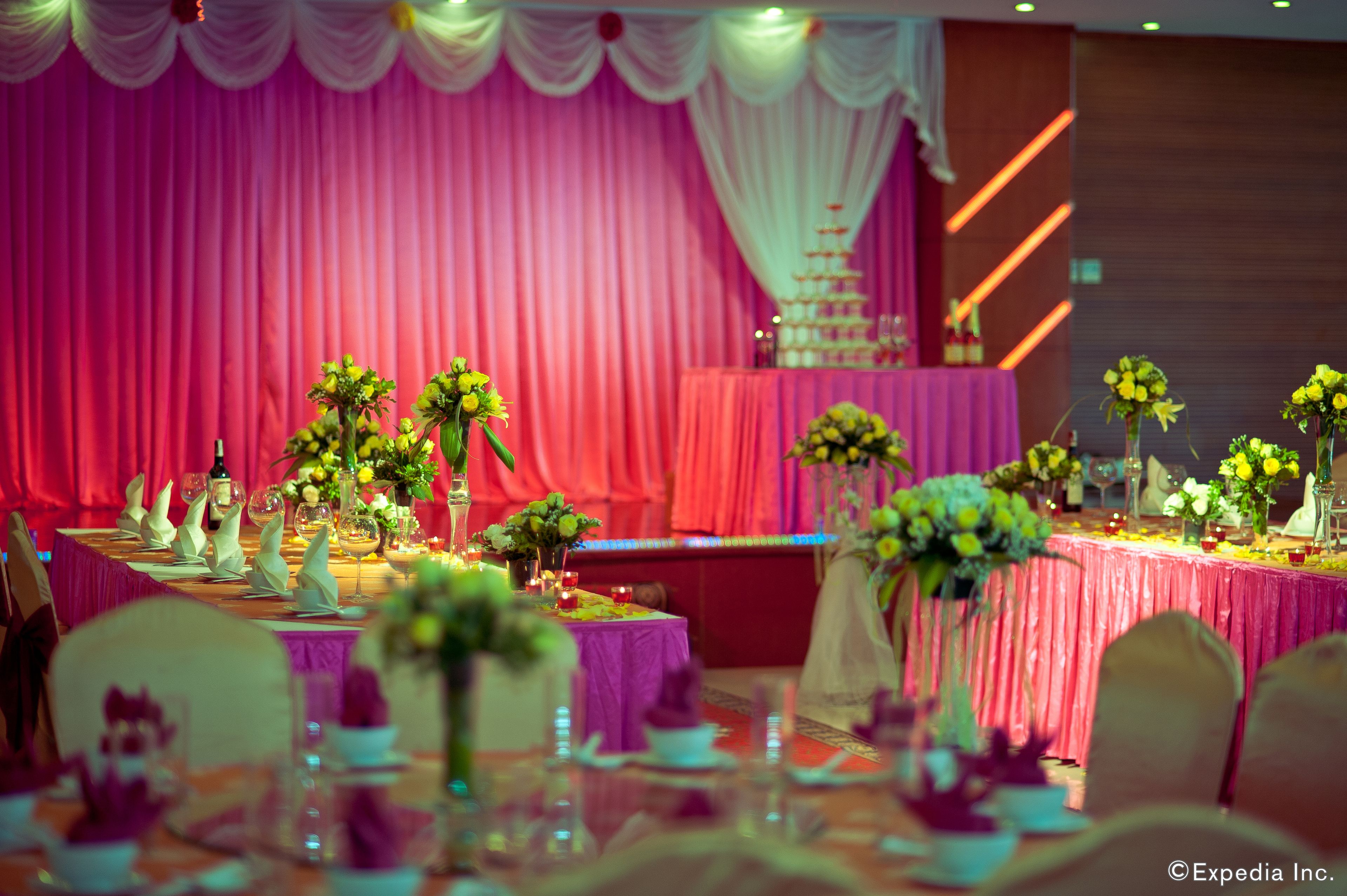 Une salle de banquet où les tables sont dressées pour un événement formel, avec des compositions florales en guise de centre de table et un gâteau à étages placé sur une scène.