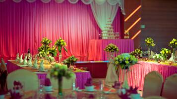 Une salle de banquet où les tables sont dressées pour un événement formel, avec des compositions florales en guise de centre de table et un gâteau à étages placé sur une scène.